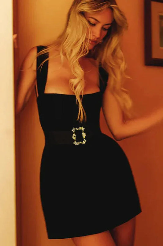 Woman in a black velvet mini dress with a square neckline and decorative gold buckle belt
