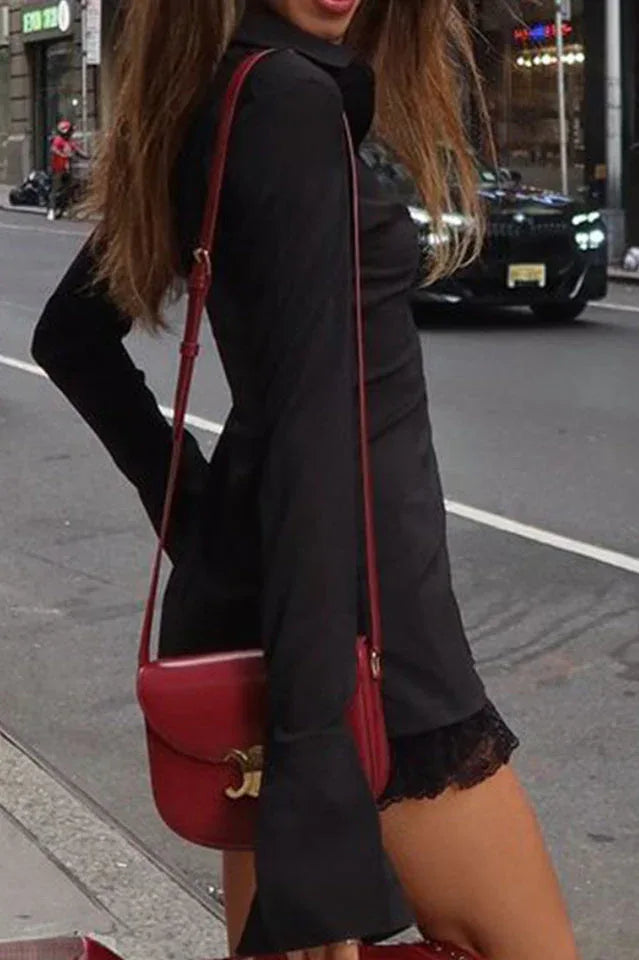 Side view of a woman wearing a black collared shirt with a lace trim hem and a red crossbody bag, on a city street.
