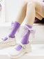 Close-up of purple ribbed socks with large, embellished bows around the calf area, worn with white Mary Jane shoes.