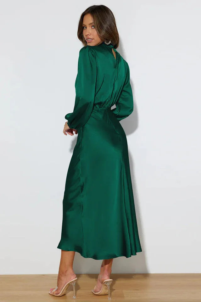 Full-length back view of a woman in an emerald green satin dress with a cowl neckline and long puff sleeves.