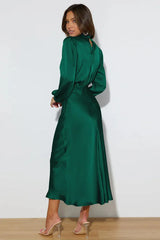 Full-length back view of a woman in an emerald green satin dress with a cowl neckline and long puff sleeves.