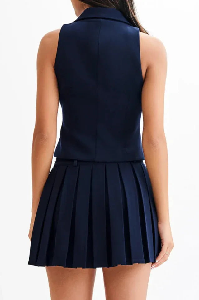 Back view of a woman wearing a navy blue sleeveless blazer vest and pleated skirt.