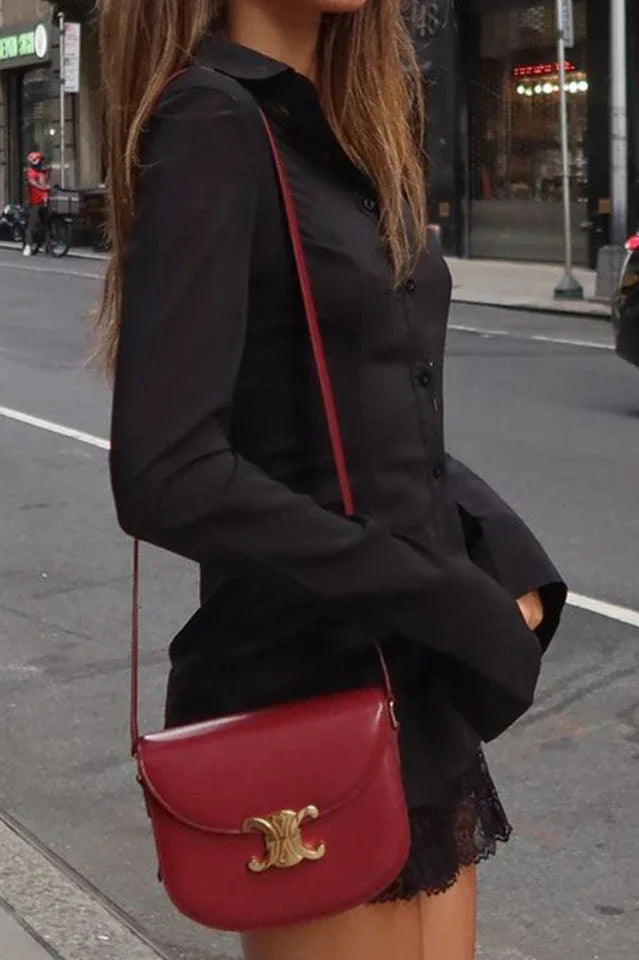 Close-up of a woman wearing a black collared shirt with a lace trim hem and a red crossbody bag.