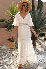 Woman wearing a white lace-trimmed maxi dress, straw hat, and sunglasses, holding a woven basket with flowers.
