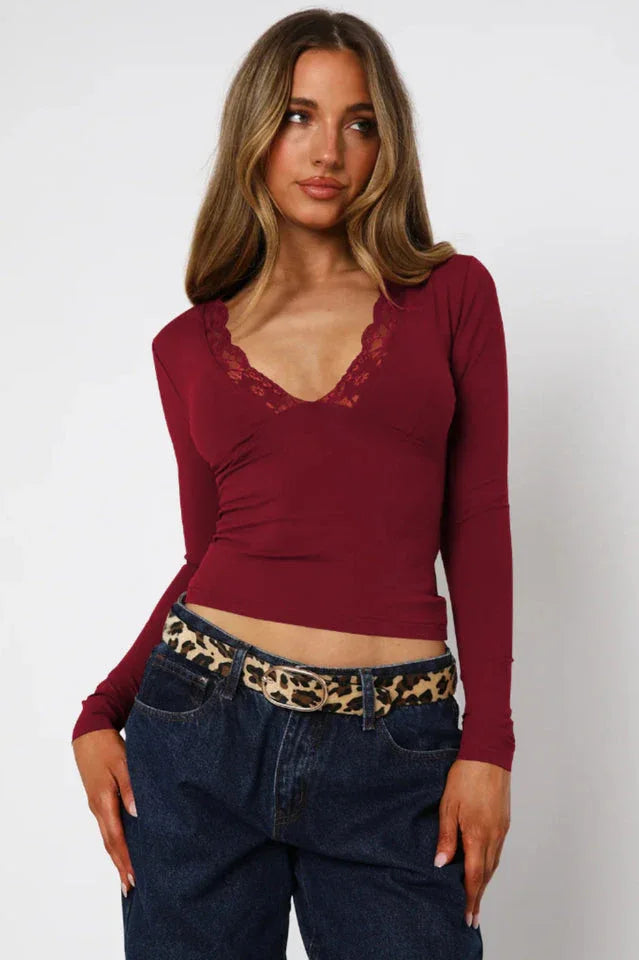 Woman wearing a burgundy long-sleeve top with lace trim, dark wash jeans, and a leopard print belt.