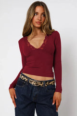 Woman wearing a burgundy long-sleeve top with lace trim, dark wash jeans, and a leopard print belt.