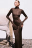 Woman wearing a long-sleeved, brown, mock neck, floor-length dress with a draped knot detail at the waist, standing next to a white horse.