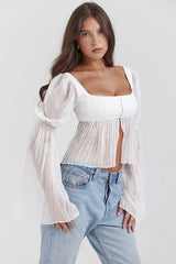 Side profile of a woman showcasing the sheer bell sleeves of a white cropped top