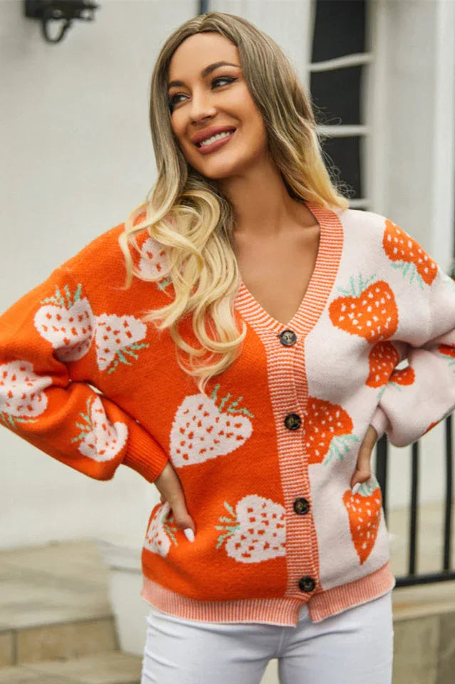 Woman smiling and wearing an orange and pink colorblock strawberry print knit cardigan.