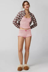 Woman wearing a pink ribbed knit tank top and shorts set with ruffle trim, layered with an open plaid shirt and slippers.