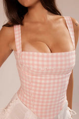 Close-up of a woman wearing a pink and white gingham corset top.