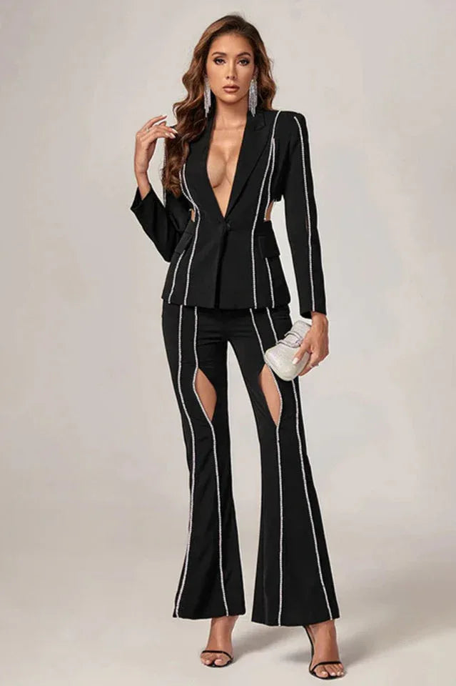 Woman in a black suit with cut-out details and decorative trim, posing with hand on hip.