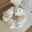 A white crocheted scrunchie with a decorative label on a white surface