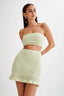 Woman wearing a light green crocheted tube top and mini skirt, front view