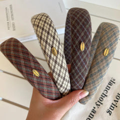 A hand holding four plaid padded headbands in different colors