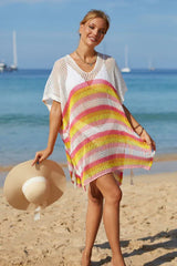 Woman in a white crochet knit kaftan with pink and yellow stripes standing on the beach