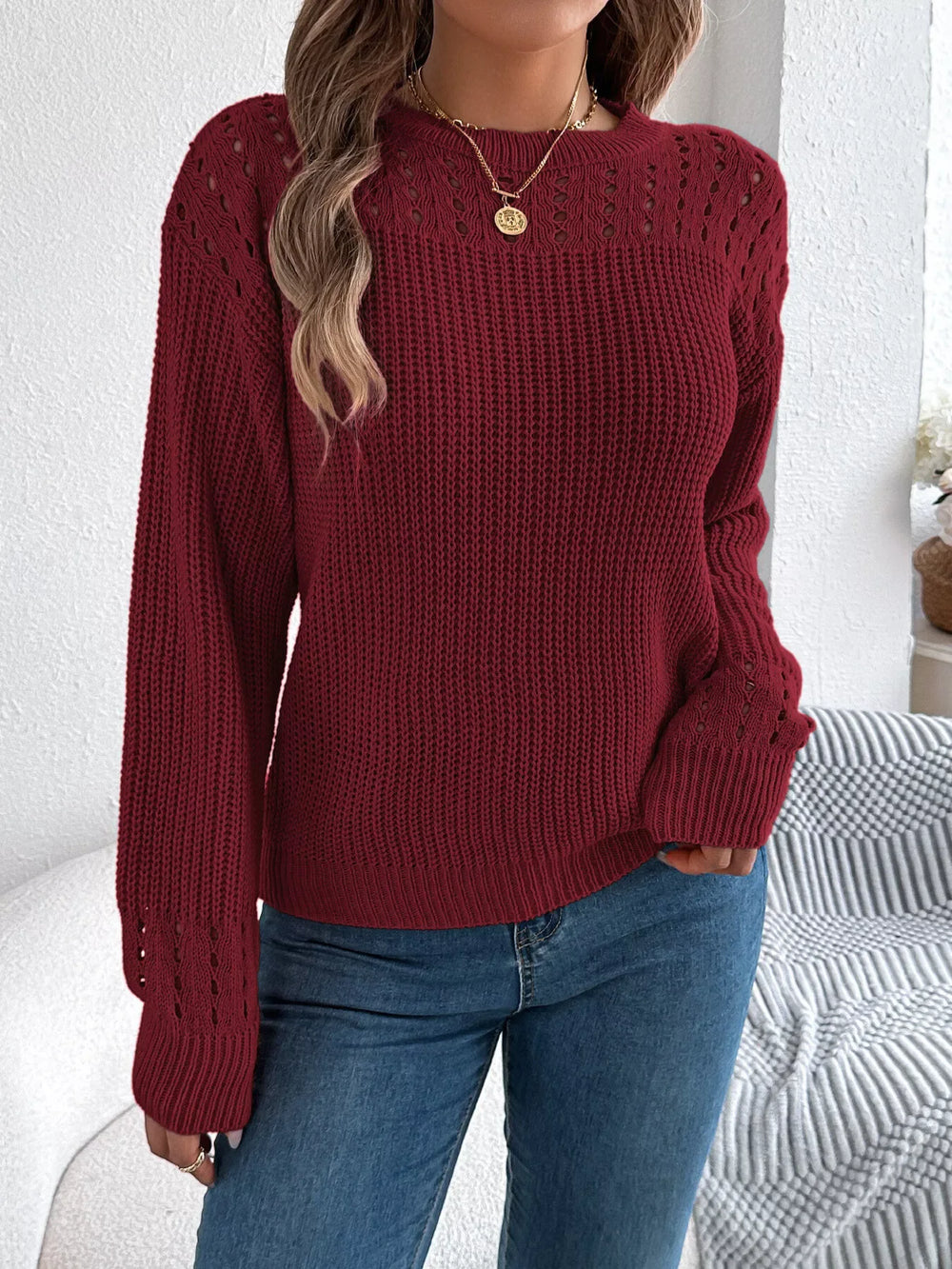 Front view of a woman wearing a maroon knit sweater with open-knit detailing and blue jeans