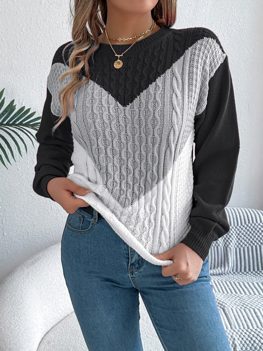 Woman wearing a black, grey, and white color block chevron cable knit sweater with blue denim jeans.