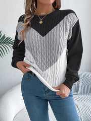 Woman wearing a black, grey, and white color block chevron cable knit sweater with blue denim jeans.