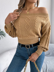 Back view of a woman wearing a tan off-the-shoulder cable knit cropped sweater and blue jeans.