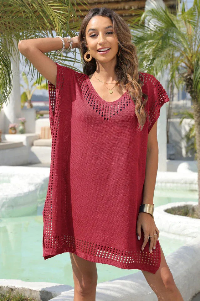 Woman wearing a red knit tunic with V-neck and crochet details, posing with arm raised