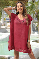 Woman wearing a red knit tunic with V-neck and crochet details, posing with arm raised