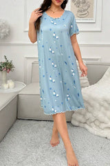 Woman standing and wearing a light blue floral print nightgown with scalloped trim.
