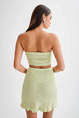 Woman wearing a light green crocheted tube top and mini skirt, back view