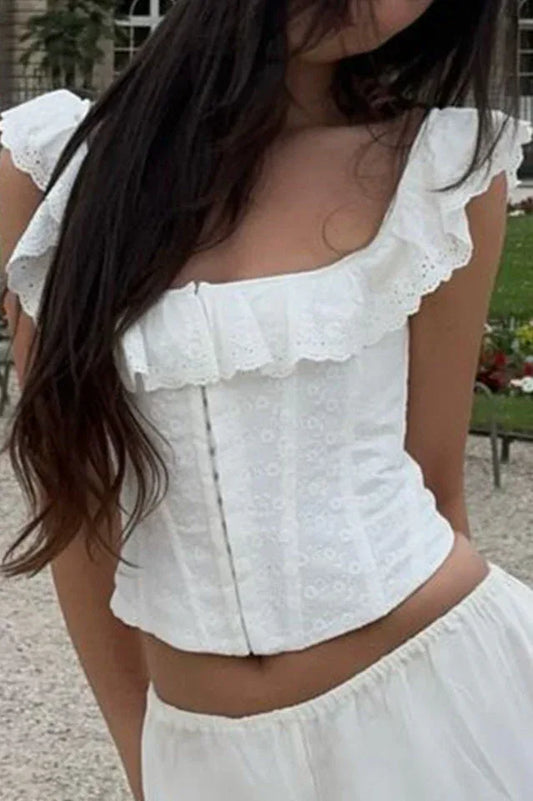 Woman wearing a white embroidered corset top with ruffled cap sleeves and a square neckline, outdoors.