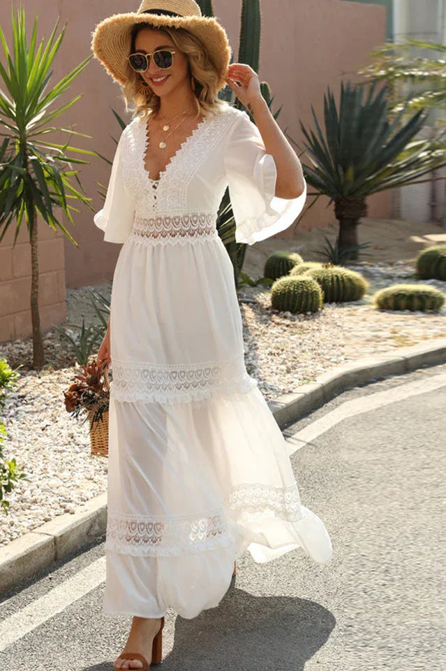 Woman in a white lace-trimmed maxi dress and straw hat walking outdoors on a paved path.