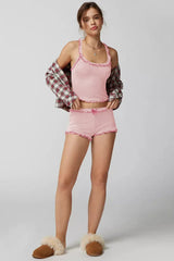 Woman wearing a pink ribbed knit tank top and shorts set with ruffle trim, layered with an open plaid shirt and slippers.