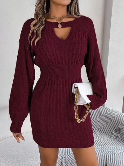 Woman wearing a burgundy cable knit sweater dress with a keyhole neckline and bishop sleeves, holding a white clutch.