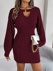 Woman wearing a burgundy cable knit sweater dress with a keyhole neckline and bishop sleeves, holding a white clutch.