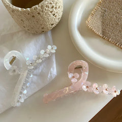 Close-up view of two floral claw hair clips, one white and one pink, on a white surface with decorative items.