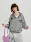 A young woman poses in a grey zip-up hoodie with a graphic print, wearing a white lace top underneath and a long white skirt.