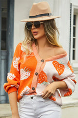 Woman wearing an orange and pink colorblock strawberry print knit cardigan with a V-neckline and button-up closure.