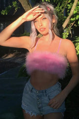 Woman in a pink fuzzy crop top and denim shorts shielding her eyes from the sun