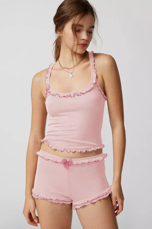 Woman wearing a pink ribbed knit tank top and shorts set with ruffle trim and a bow accent.