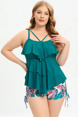Woman wearing a teal ruffled tankini top with floral print swim shorts, front view.