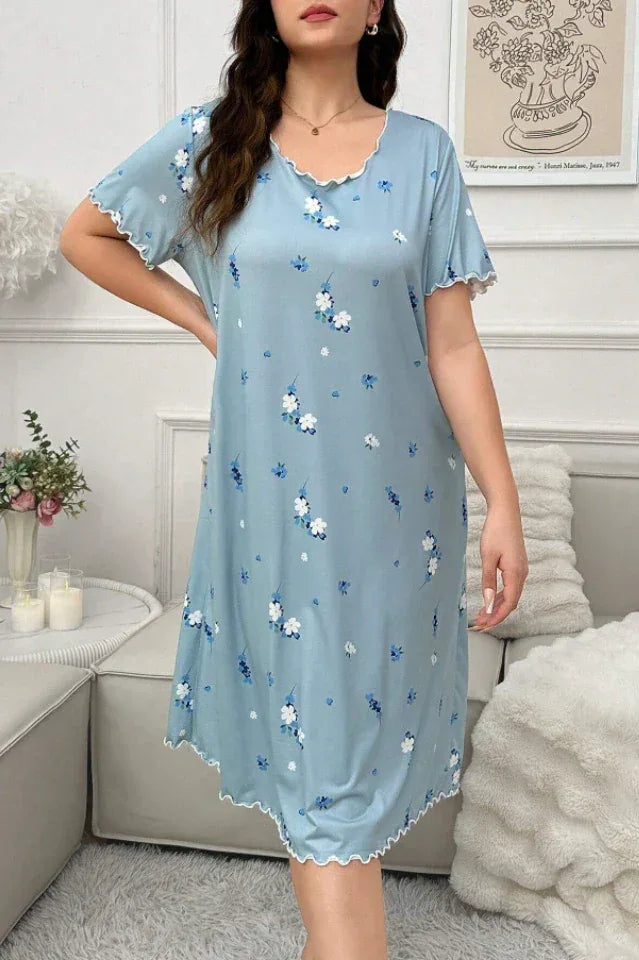 Close-up of a woman wearing a light blue floral print nightgown with scalloped trim, sitting on a sofa.