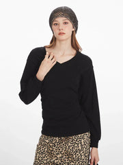 Close-up of a woman wearing a black V-neck long-sleeved top, adjusting her grey knit beanie.
