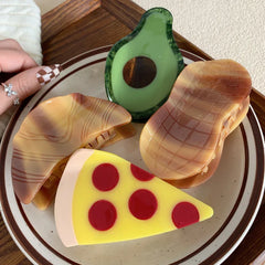 A hand with checkered nail art reaches for a collection of food-themed hair clips, including a pizza slice.