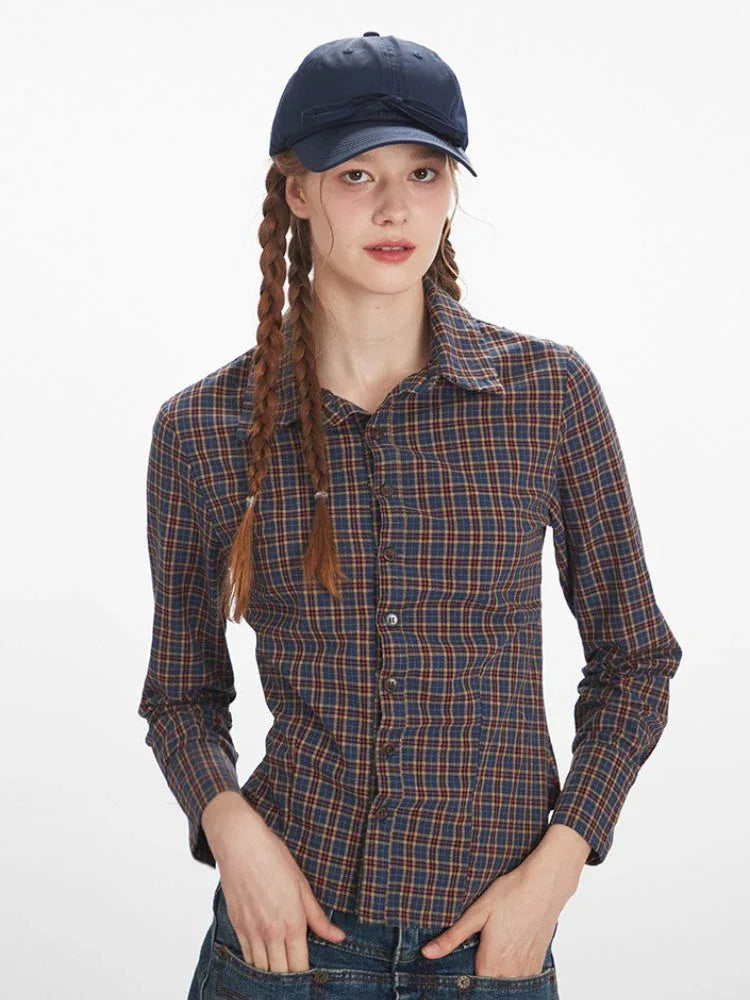 Close-up front view of a woman's upper body wearing a plaid button-down shirt and a baseball cap.