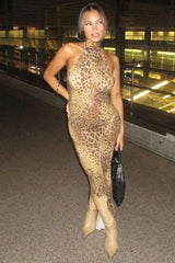 Woman posing in a leopard print halter neck maxi dress with tan boots and a black handbag