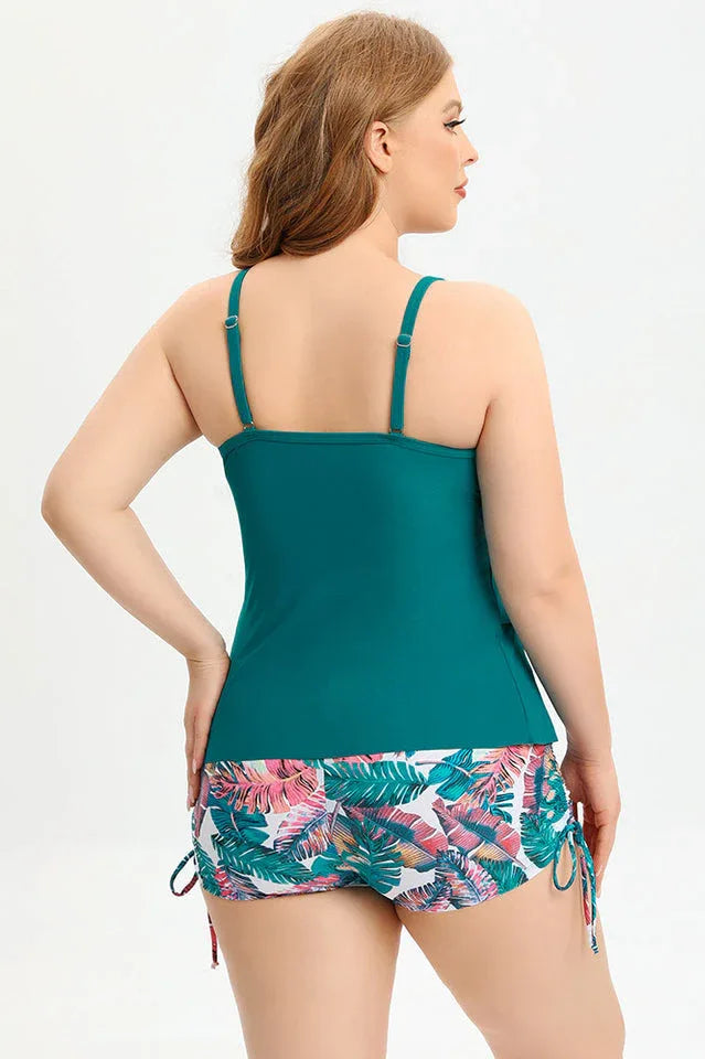 Woman wearing a teal ruffled tankini top with floral print swim shorts, back view.