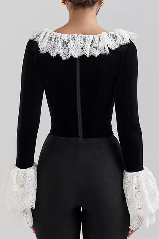 Woman wearing a black velvet top with white lace trim and ruffled collar and cuffs, back view