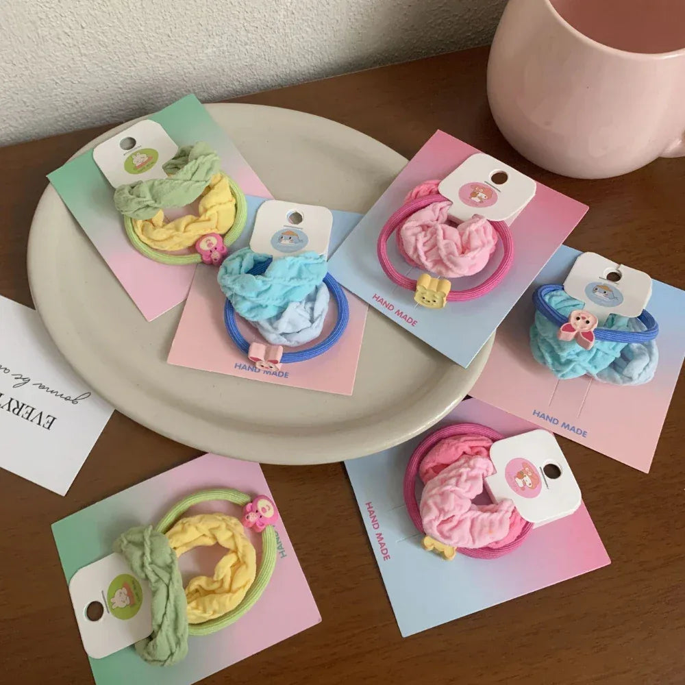 Overhead view of several scrunchie sets displayed on a plate and a wooden table, featuring pastel colors and animal charms.