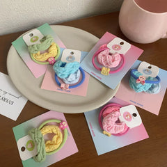 Overhead view of several scrunchie sets displayed on a plate and a wooden table, featuring pastel colors and animal charms.