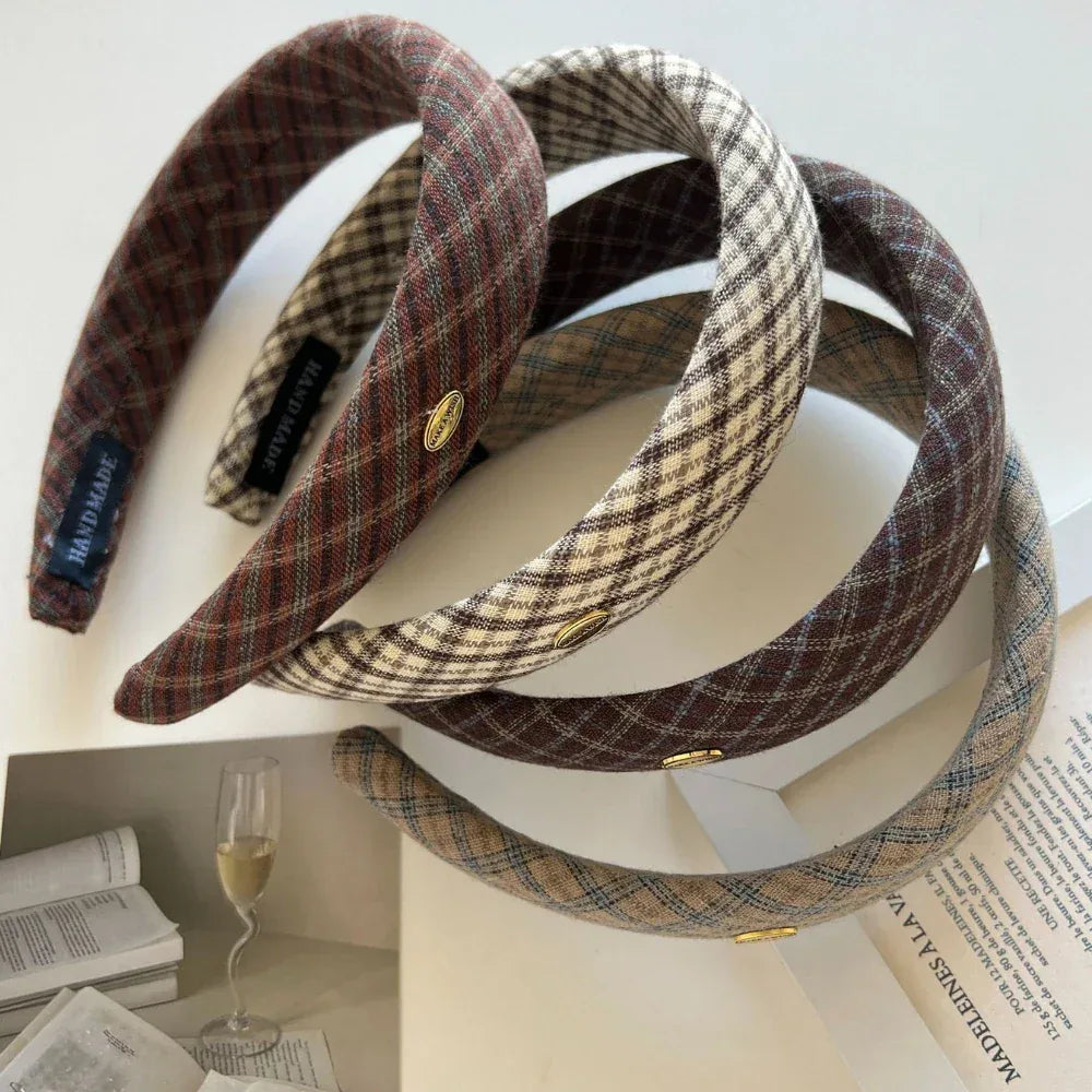 A close-up of several plaid padded headbands with a glass of champagne in the background