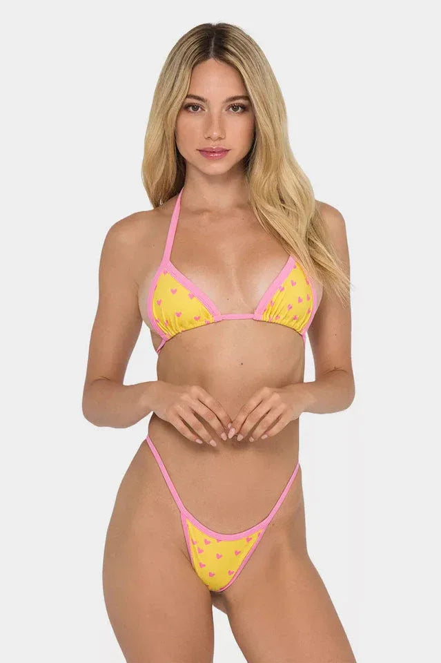 Woman wearing a yellow bikini with pink heart print and pink trim.